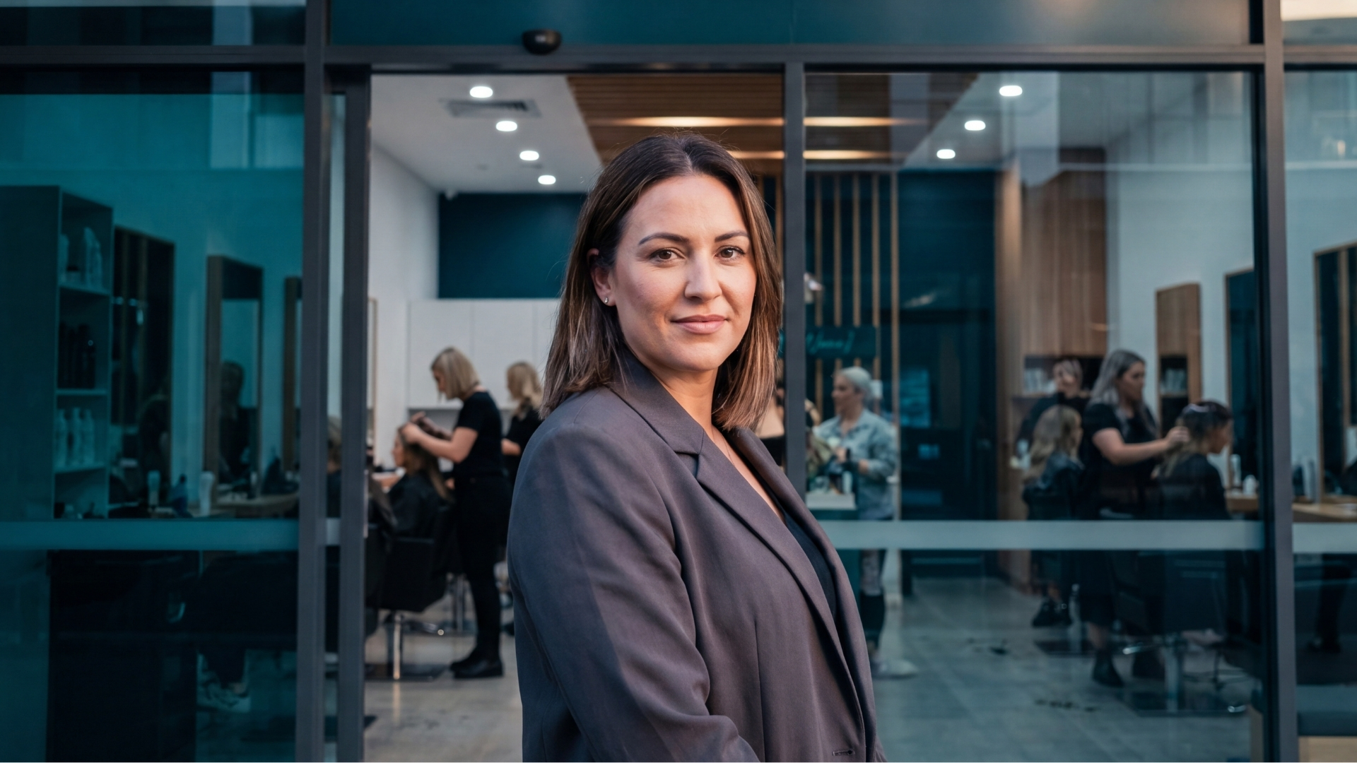 A confident salon owner standing in front of her busy hair salon while her team works with clients