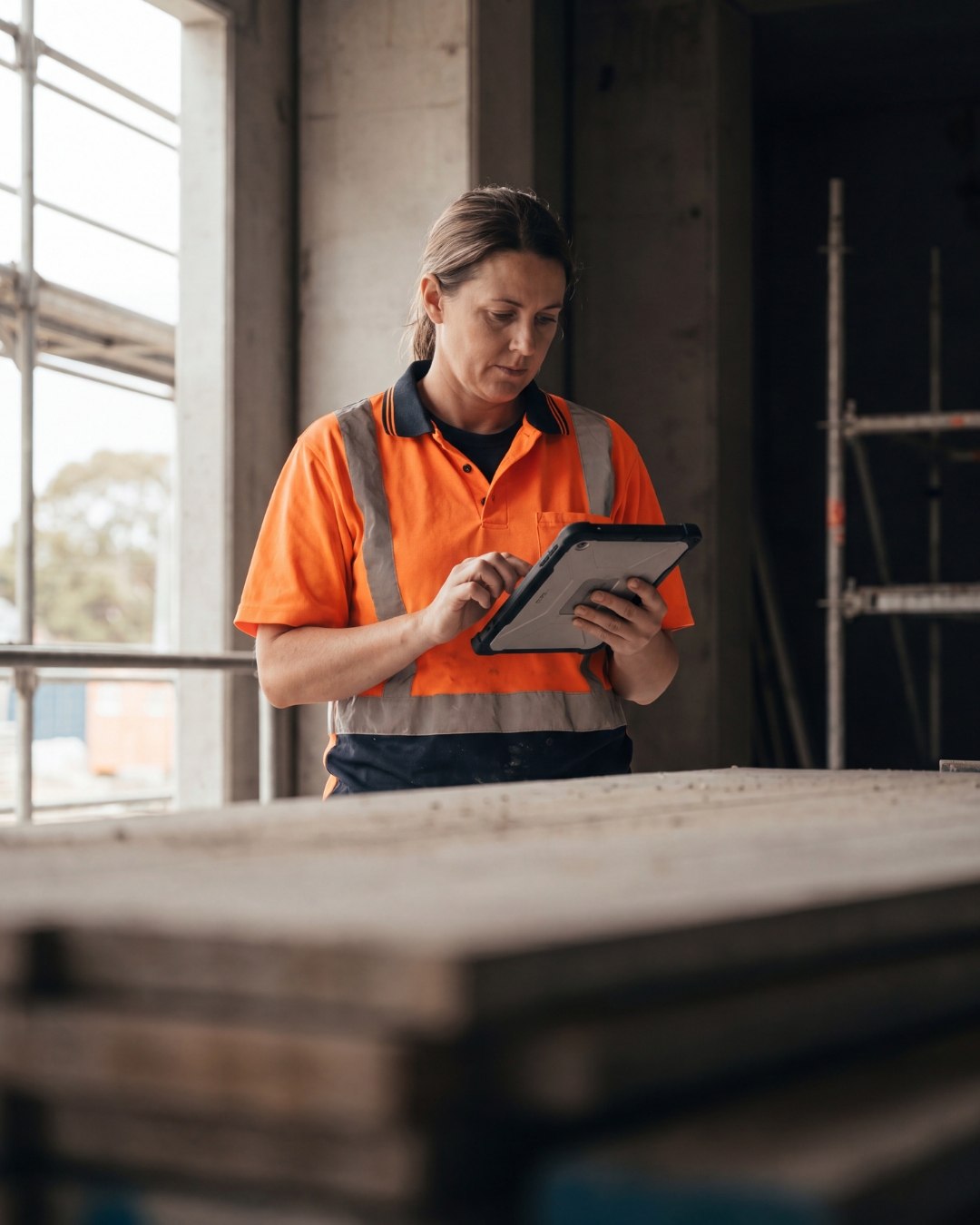 A tradeswoman on a construction site reviewing her numbers on a tablet